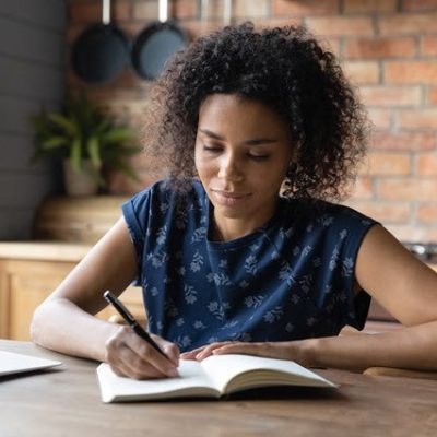 Woman writing resolutions on notebook next to laptop